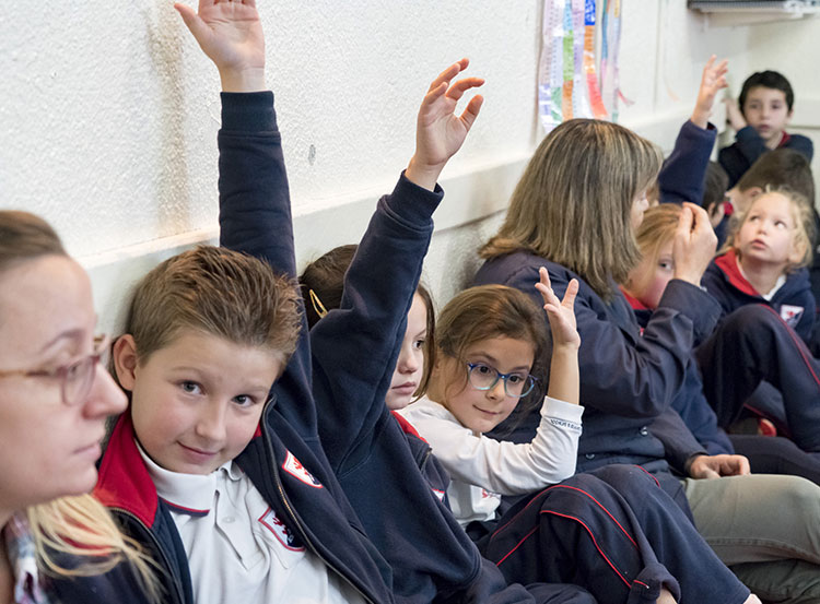 niños en clase levantando las manos para responder preguntas